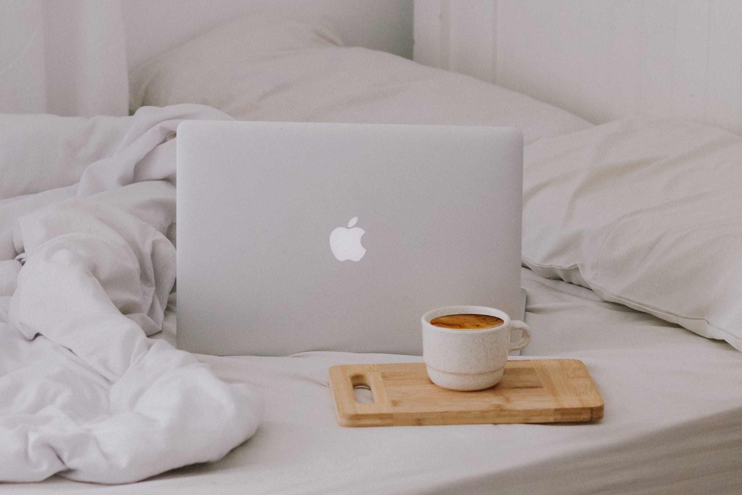 A MacBook resting on a bed with a hot drink.